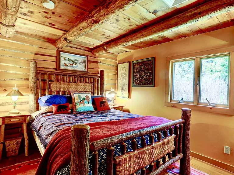 Master Bedroom with live edged wood paneling, queen sized bed with Hickory frame, twig side tables with brass lamps and double casement windows.