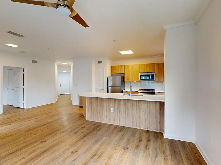 Apartment kitchen with stainless steel appliances, dining and living room with wood style floor.