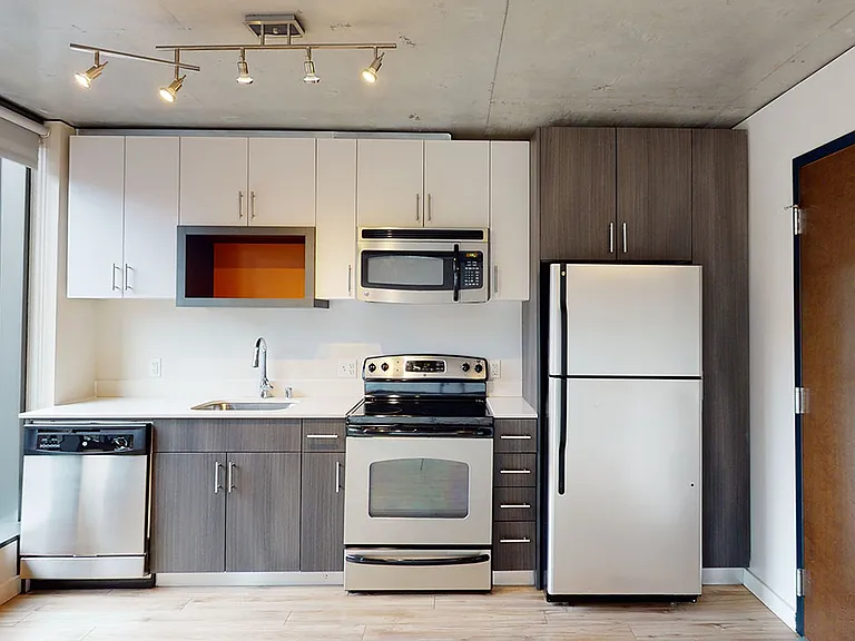 Apartment kitchen with stainless steel appliances, quartz countertops and wood-style flooring.