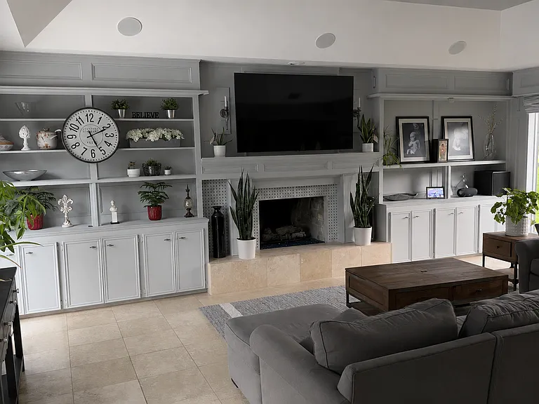 Large living room with floor to ceiling windows on the North and South side of the room, a tray ceiling with built-in cabinetry and shelving around the fireplace.