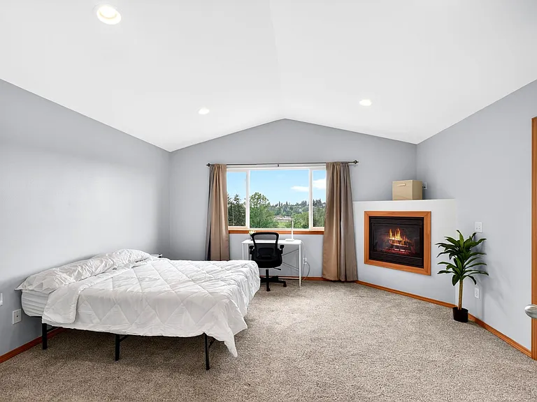 Spacious bedroom with a large picture window, dedicated desk nook, and a built-in fireplace for added comfort.