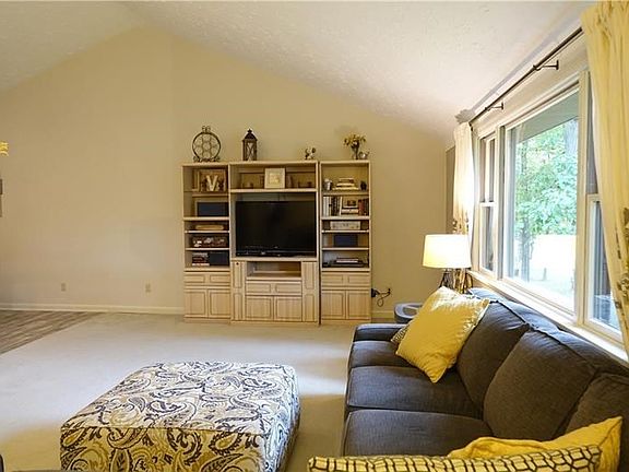 Living room with 3 way gas fireplace, vaulted ceiling, and newer carpeting