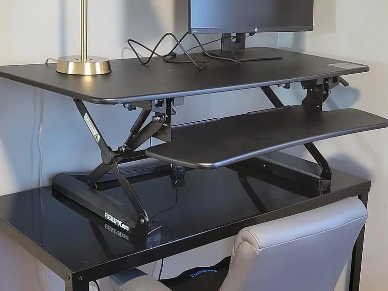 Work station in second bedroom which includes a sit-stand desk, desk chair, and monitor.