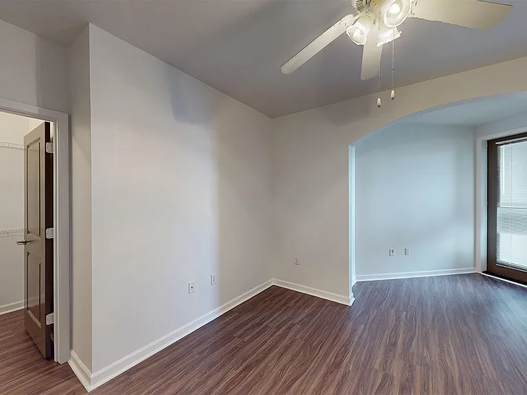 Spacious apartment bedroom with large closet, attached bathroom and wood-style flooring.