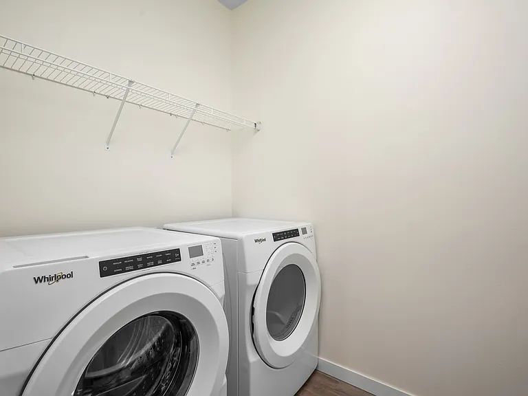 Modern laundry area featuring top-loading washer and dryer with overhead wire shelving. Modern laundry area featuring top-loading washer and dryer with overhead wire shelving.