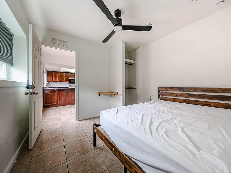 Private bedroom with tile flooring, ceiling fan, and an open closet; convenient access to the kitchen just outside.