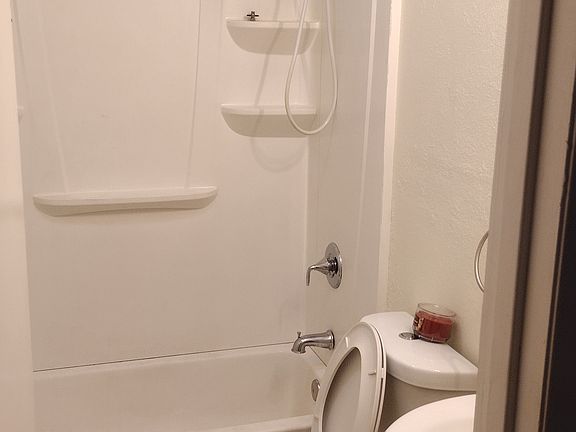 Main bathroom has built in hamper and shelfs behind door. Bathtub and shower. Large oval shaped toilet.