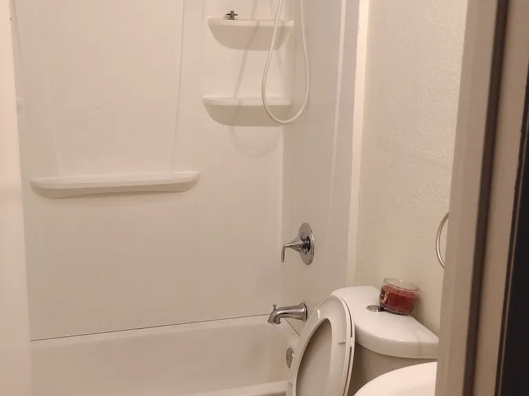 Main bathroom has built in hamper and shelfs behind door. Bathtub and shower. Large oval shaped toilet.