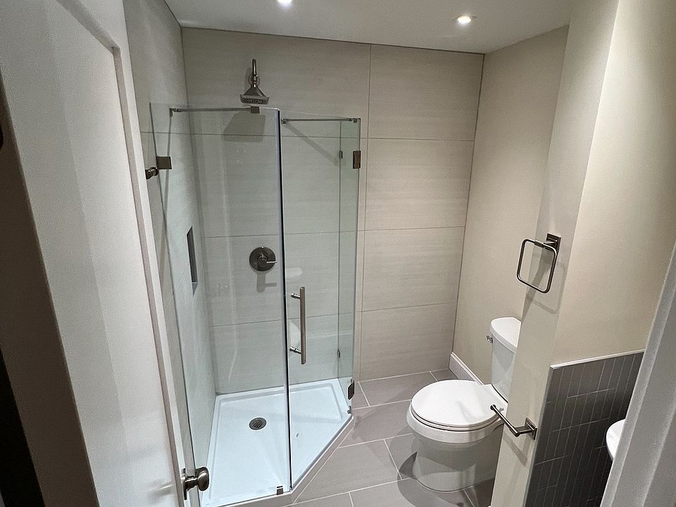 This renovated bathroom features a frameless glass shower, sleek tile flooring, a modern pedestal sink, and an LED mirror cabinet. Clean lines and quality finishes offer a stylish, space-efficient design perfect for everyday modern comfort.