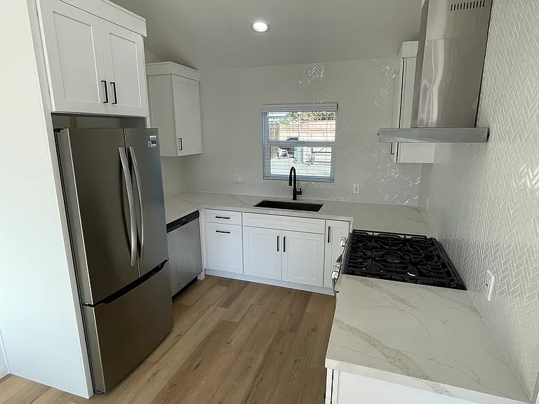 Updated kitchen featuring stainless steel appliances, quartz countertops, white shaker cabinets, and a sleek tile backsplash.