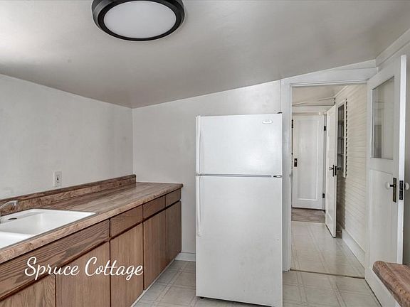 Another view of kitchen. Refrigerator is shown. Entrance to mud room shown, with the bathroom beyond the mud room.