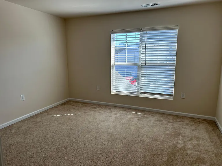A view from within bedroom 2, looking out from the closet. The door to the room is to the left. This room faces the front of the house, where you can see a red truck parked in the overflow parking lot immediately across from the driveway. There are severa