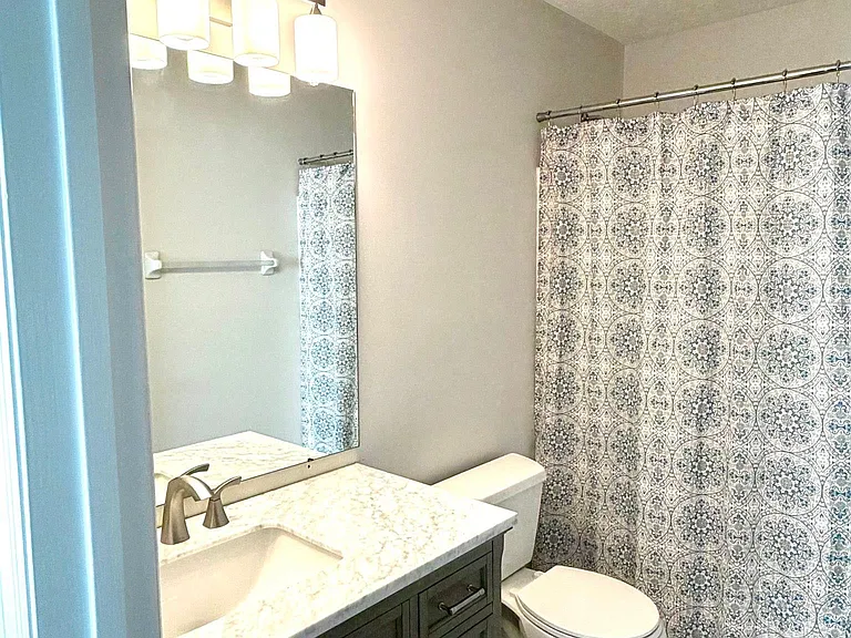 Shared hall bath with tub/shower combo and new marble-topped vanity and lighting.