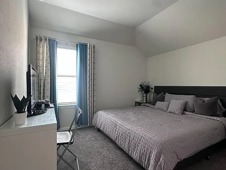 Bedroom with carpet flooring, a window with curtains, and space for a bed plus a desk or TV setup.