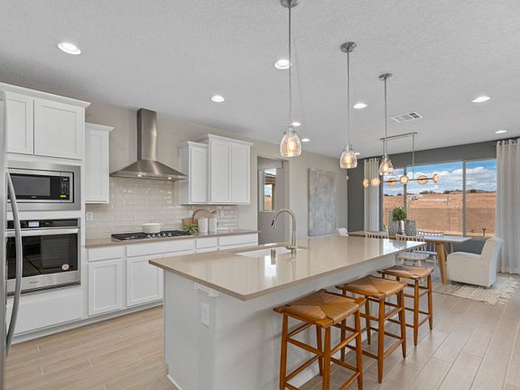 A designer Chef kitchen layout with white cabinetry, built-in appliances and pendant lighting.