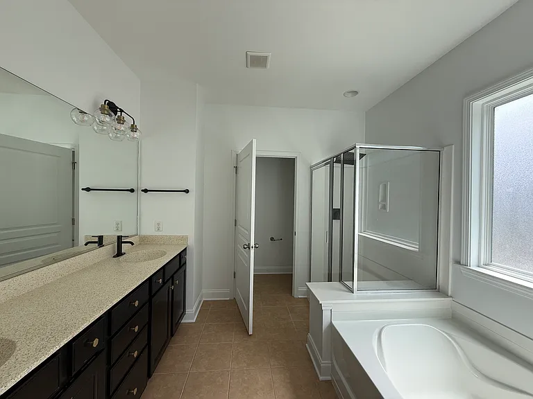 Luxurious master bathroom complete with dual sinks, an abundance of vanity cabinet storage, chic modern vanity lighting, a separate shower, and a relaxing tub under a privacy-frosted window."