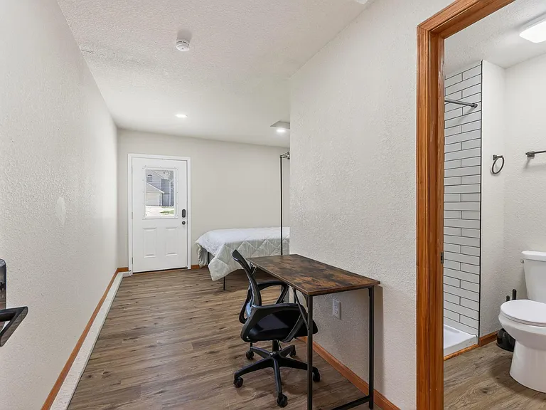 Private bedroom with durable flooring, an exterior door for easy access, and space for a desk plus adjacent bath.
