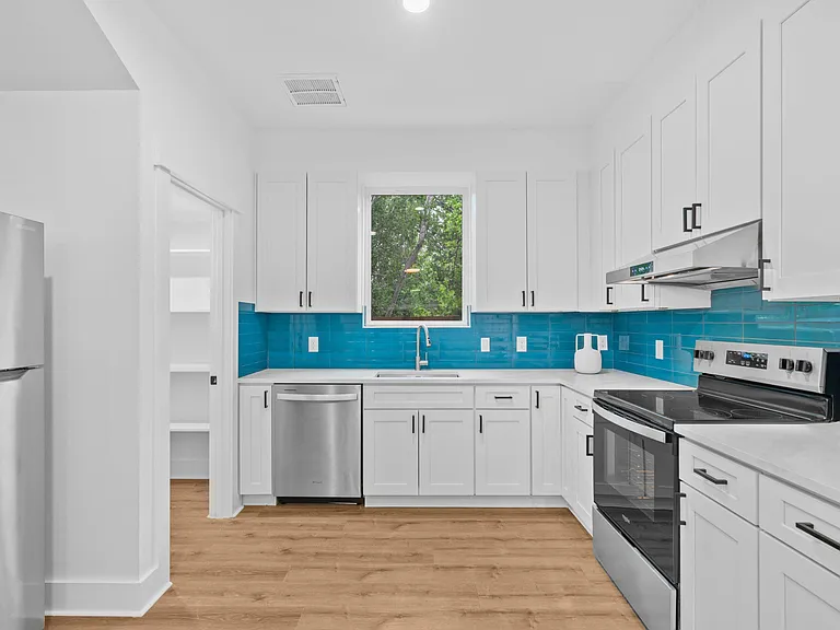 Updated kitchen with ample shaker cabinetry, pantry storage, stainless appliances, and a sink set under a large window.