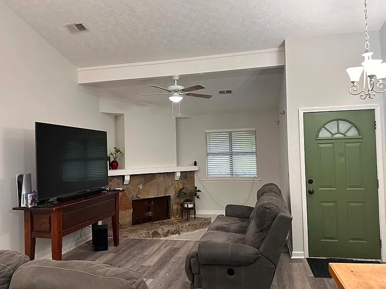Step into a bright and inviting living space featuring soaring vaulted ceilings and a floor-to-ceiling stone fireplace that serves as the heart of the home. The spacious open-concept layout seamlessly connects the living room, dining area, and kitchen.