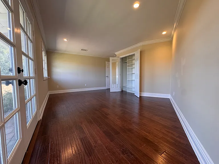 Bedroom with french doors opening to backyard + wood flooring.