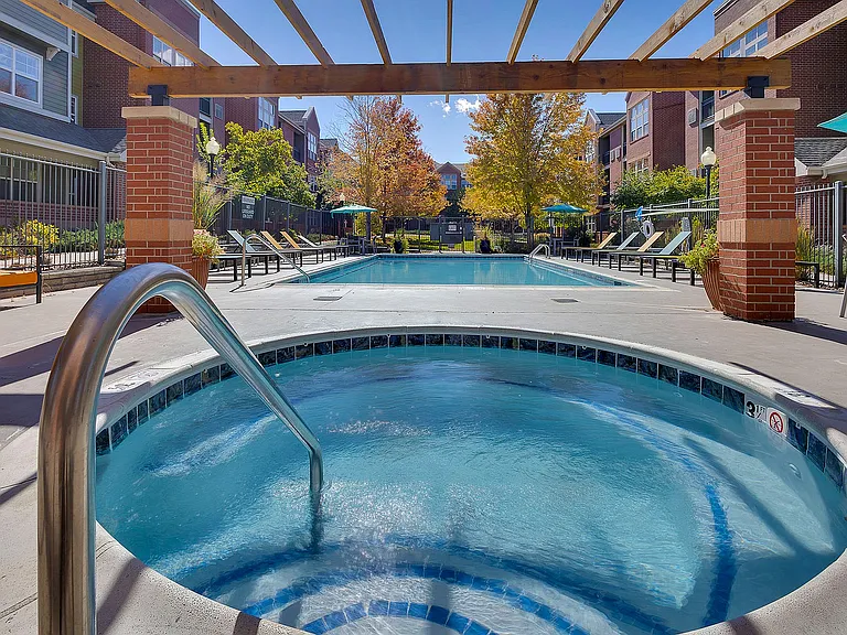 Inviting outdoor pool area with a hot tub, surrounded by comfortable lounge chairs and vibrant autumn trees, offering a perfect relaxation spot.