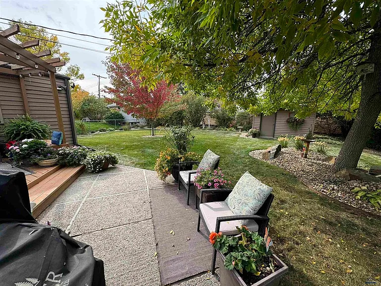 Step off of the deck onto a concrete patio area before entering the landscaped backyard.