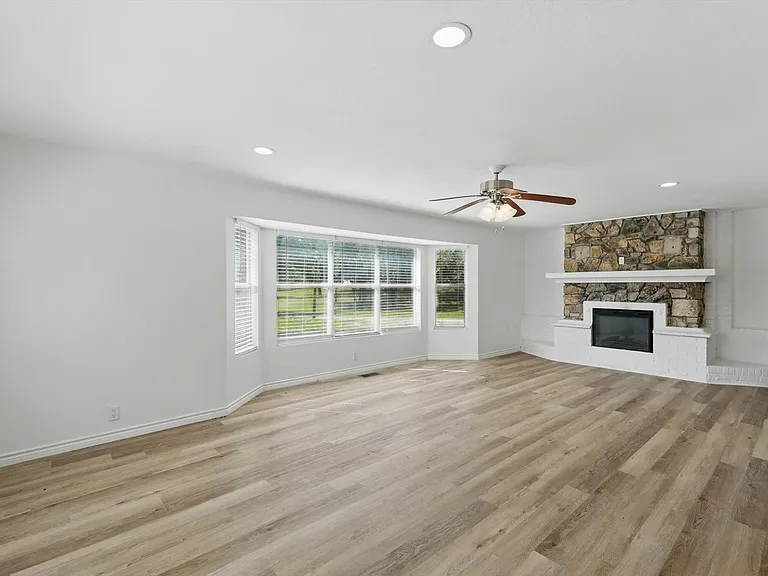 Unfurnished living room with a ceiling fan, light wood-style flooring, a stone fireplace, baseboards, and recessed lighting