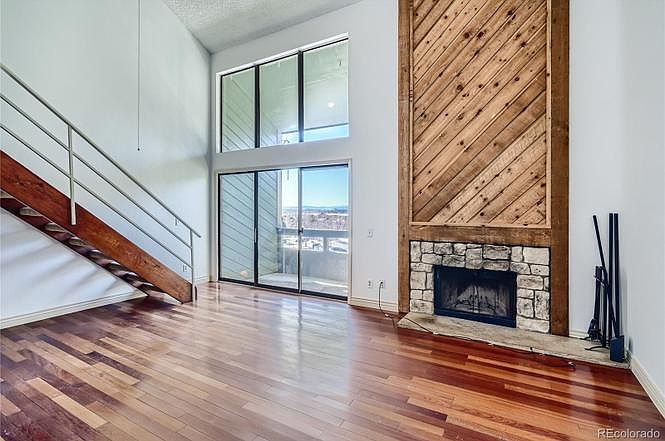 Living room with vaulted ceilings, high windows, balcony door, mountain views, fireplace, cherry wood flooring, and stairs to loft