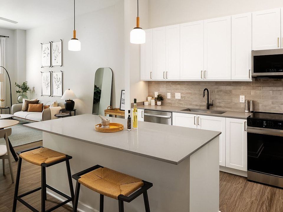 Upgrade Collection kitchen with white cabinetry, beige tile backsplash, grey quartz countertops, pendant lighting, and hard surface vinyl plank flooring (Representative photo)