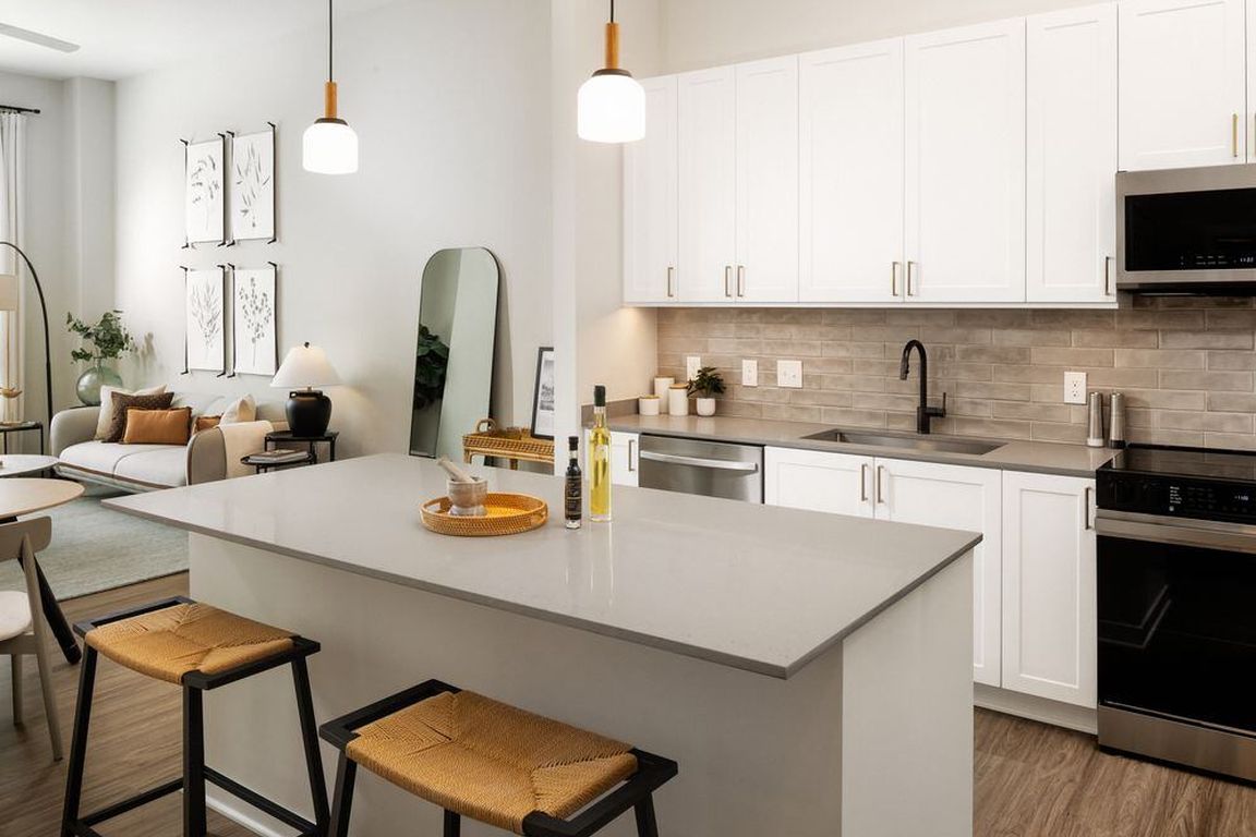 Upgrade Collection kitchen with white cabinetry, beige tile backsplash, grey quartz countertops, pendant lighting, and hard surface vinyl plank flooring (Representative photo)
