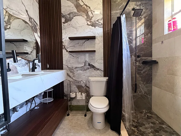Spacious bathroom with stone-look tile, a long vanity with storage, and a walk-in shower with rainfall showerhead.