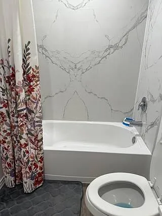 Full bathroom with a tub/shower combo, marble-look wall surround, and a patterned shower curtain for added style.