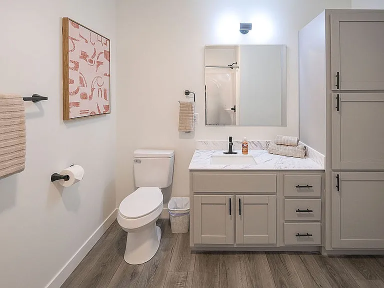 Elegant bathroom with modern fixtures, cozy lighting, and stylish cabinetry. Features a marble countertop and contemporary wall art.