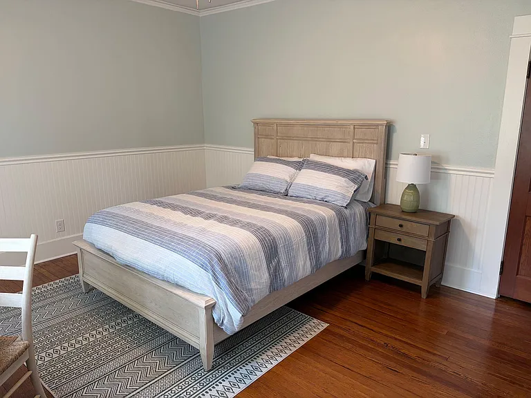 Furnished bedroom with a full bed, nightstand and lamp, wainscoting detail, and hardwood floors for easy upkeep.