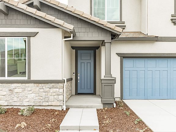 A modern, two-story house with a stone facade, a blue front door, and a matching blue garage door, s