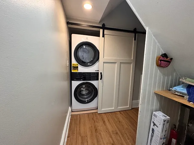Stacked washer/dryer behind the barn door. Storage area for broom and cleaning supplies.