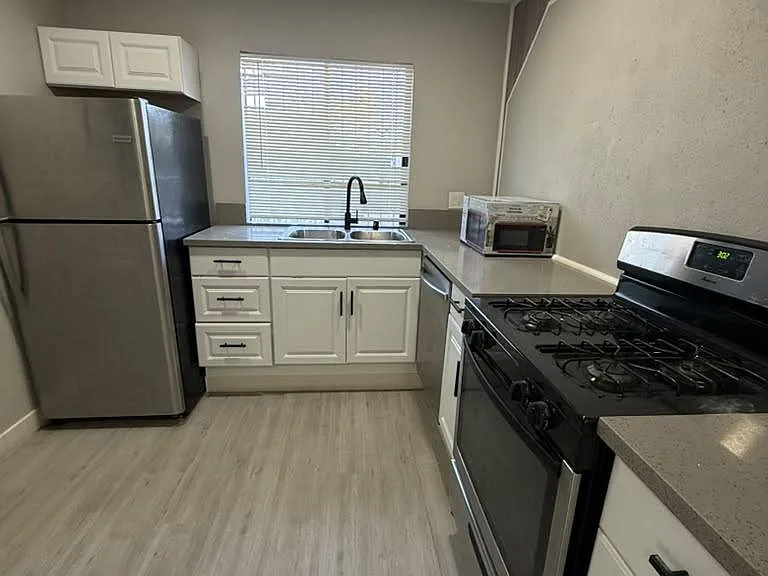 Galley kitchen with stainless steel appliances, ample cabinet storage, and a large sink set beneath a window.