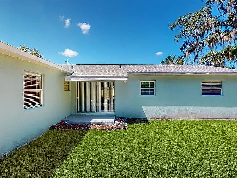 Well-maintained exterior with lush lawn, mature trees, privacy fence, and covered carport