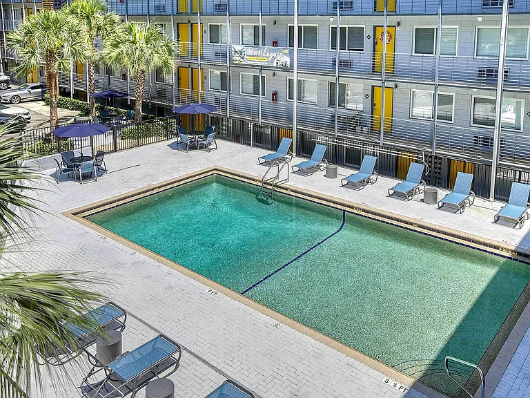 Inviting apartment courtyard featuring a sparkling swimming pool, surrounded by modern lounge chairs and vibrant yellow accents, perfect for relaxation and leisure.