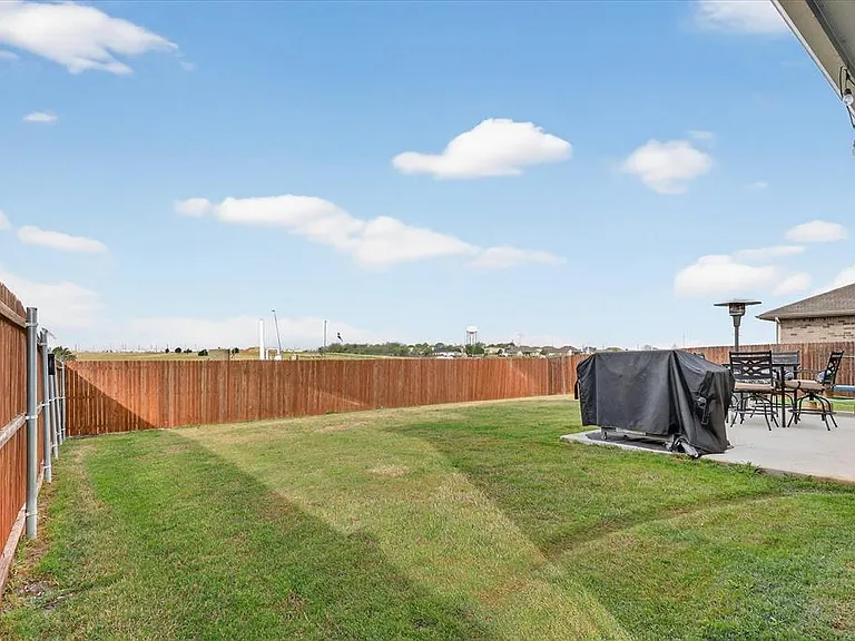 Expansive backyard featuring a manicured lawn, a full wood privacy fence, and a concrete patio