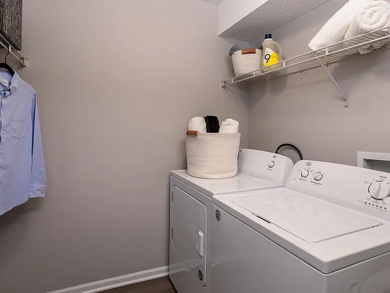 Convenient in-unit laundry facilities featuring a full-size washer and dryer, ample shelving, and hanging space.