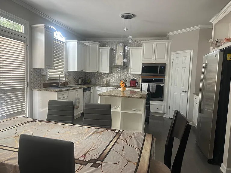 Spacious kitchen with ample white cabinetry, granite counters, center island, and stainless appliances plus adjacent dining.