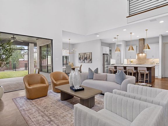 Open-concept living area with high ceilings, wood-finish flooring, and a contemporary kitchen featuring a large island, pendant lighting, and stainless steel
 appliances