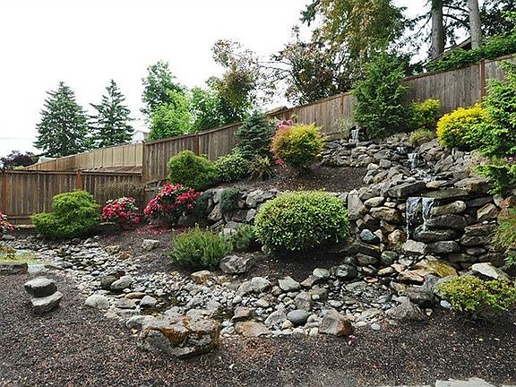Cascading rear yard serene rock waterfall and mature low maintenance landscaping