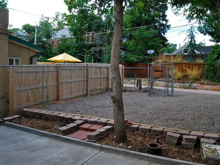 Back yard view with six foot fence on both sides and gated parking entrance.