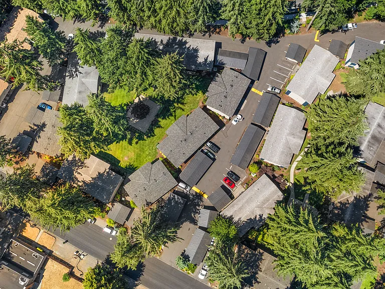 A bird's-eye view of the apartment community surrounded by mature trees, green space, residential buildings, and convenient covered parking.