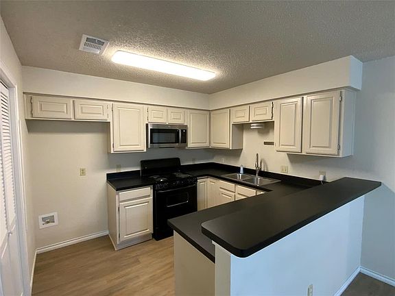 Kitchen featuring stainless steel microwave, a sink, a peninsula, dark countertops, and electric range
