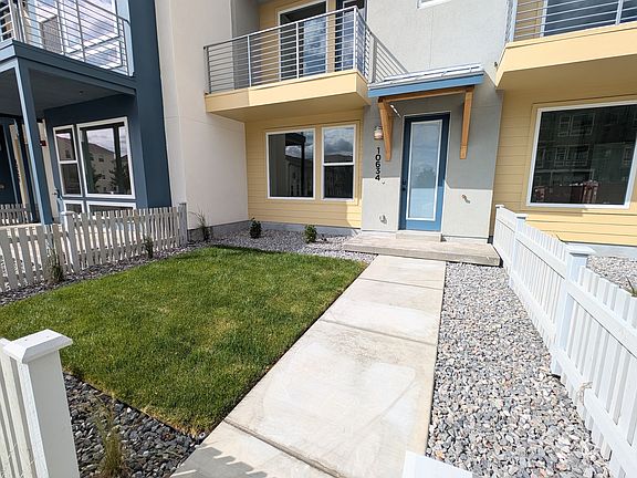 A modern townhouse with yellow and gray exterior, blue door, balconies, small front yard with green