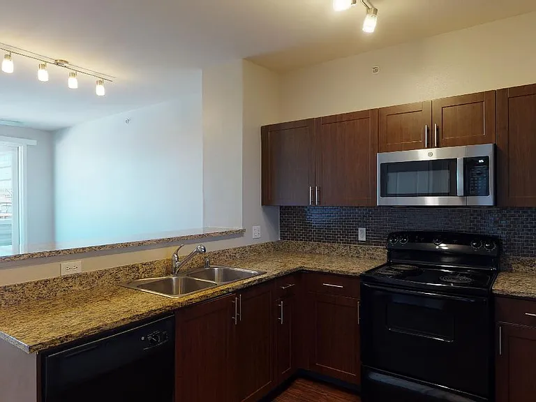 Apartment kitchen with granite countertops and wood-style flooring.