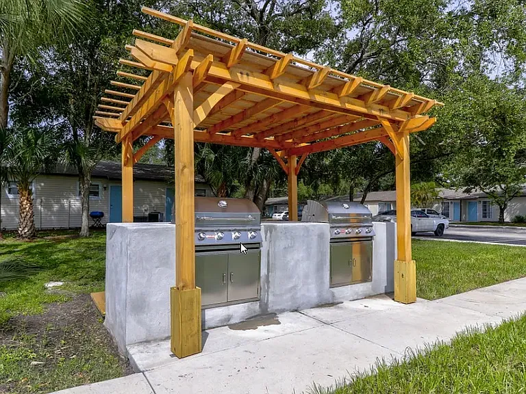 Charming outdoor grilling area with twin stainless steel barbeque stations under a stylish wooden pergola, perfect for hosting gatherings.